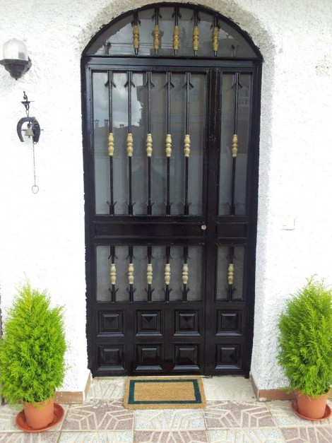 puerta de entrada a casa rural flanqueada por macetas con pinos